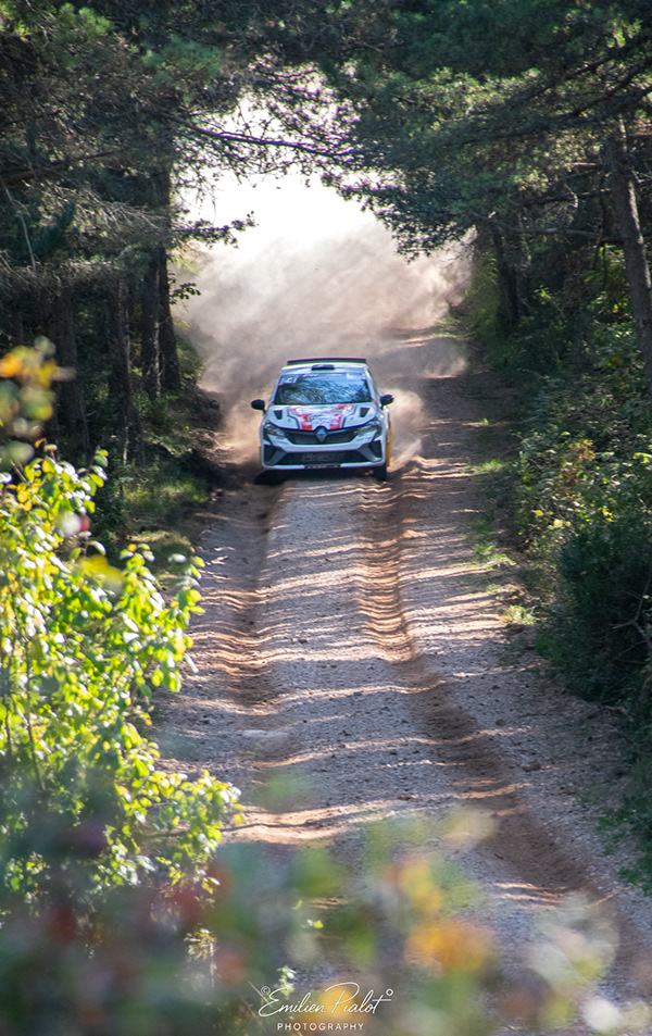 Voiture de rallye blanche et rouge dans un tunnel d'arbres, nuage de poussière