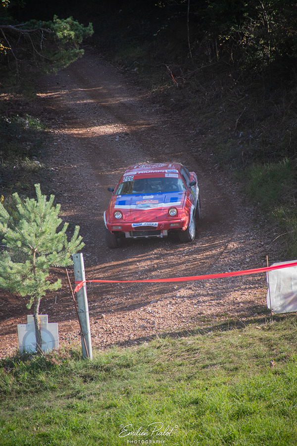 Voiture de rallye historique rouge, blanche et bleue n°206 sur chemin de terre