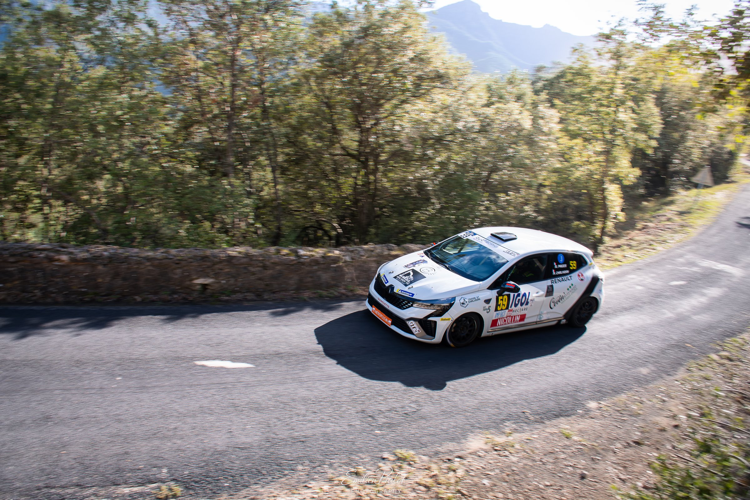 Porsche 911 GT3 Rally blanche et rouge en dérive sur route de montagne, village en fond