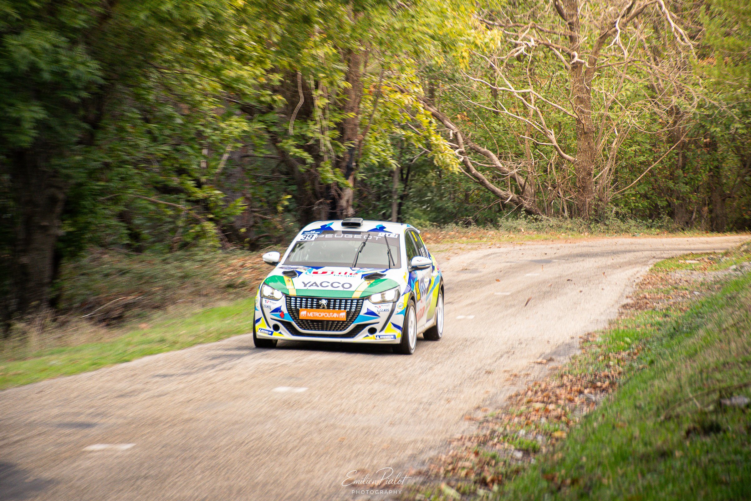 Renault Clio de rallye sur un chemin forestier, spectateur assis au bord