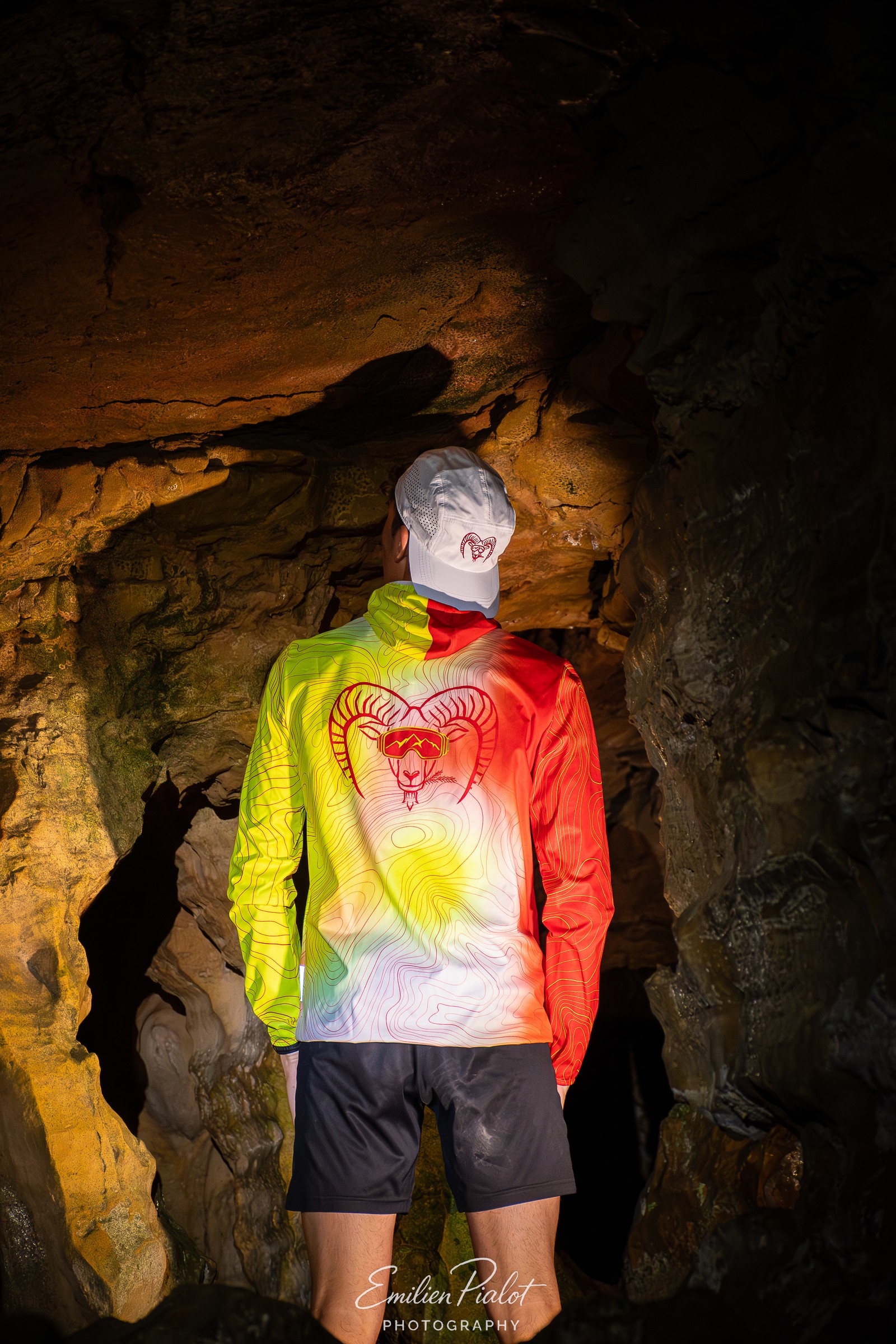 Séance Muflon en grotte, veste technique orange, éclairage dramatique