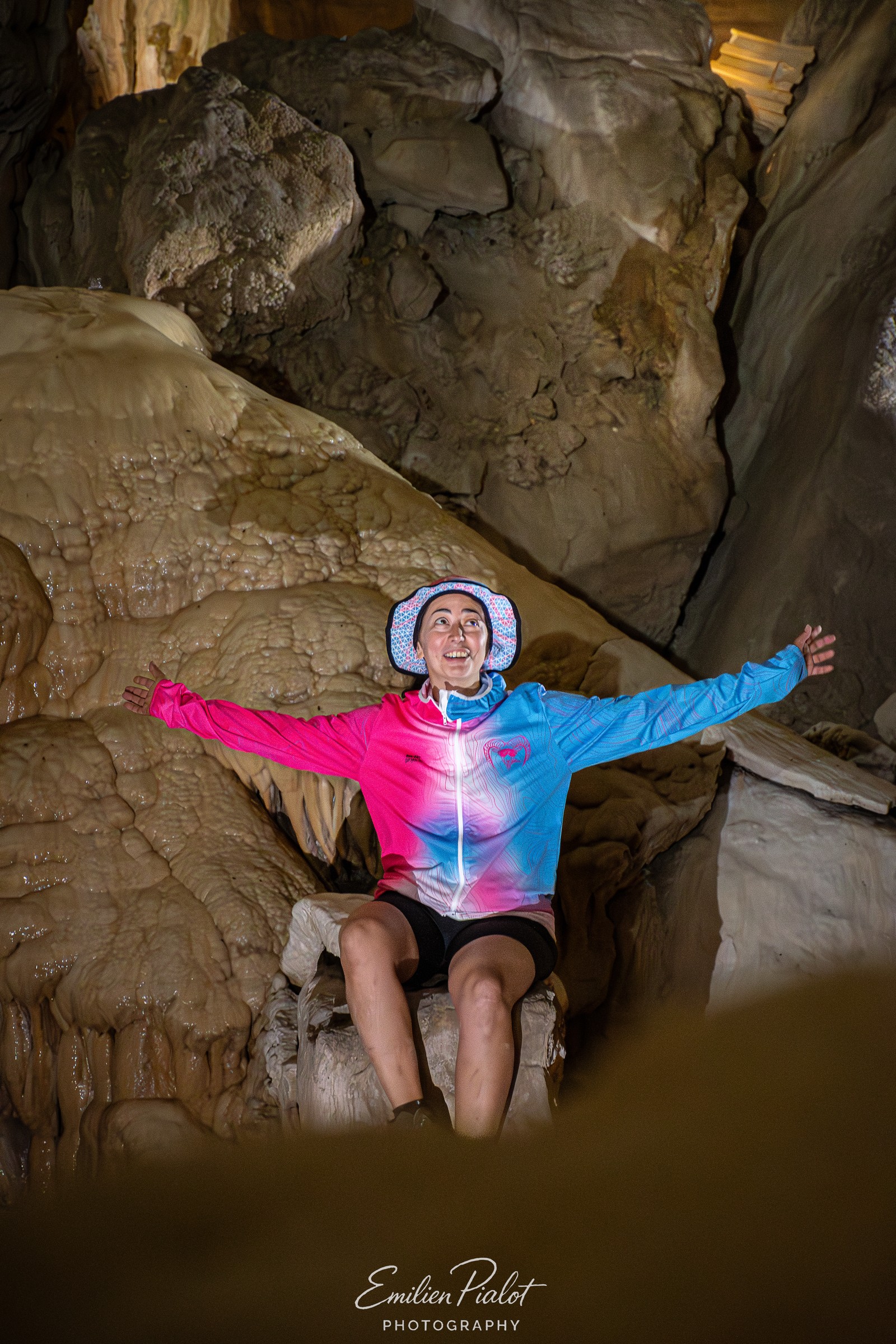 Séance Muflon en grotte, veste bleue, bras ouverts sous la lampe frontale