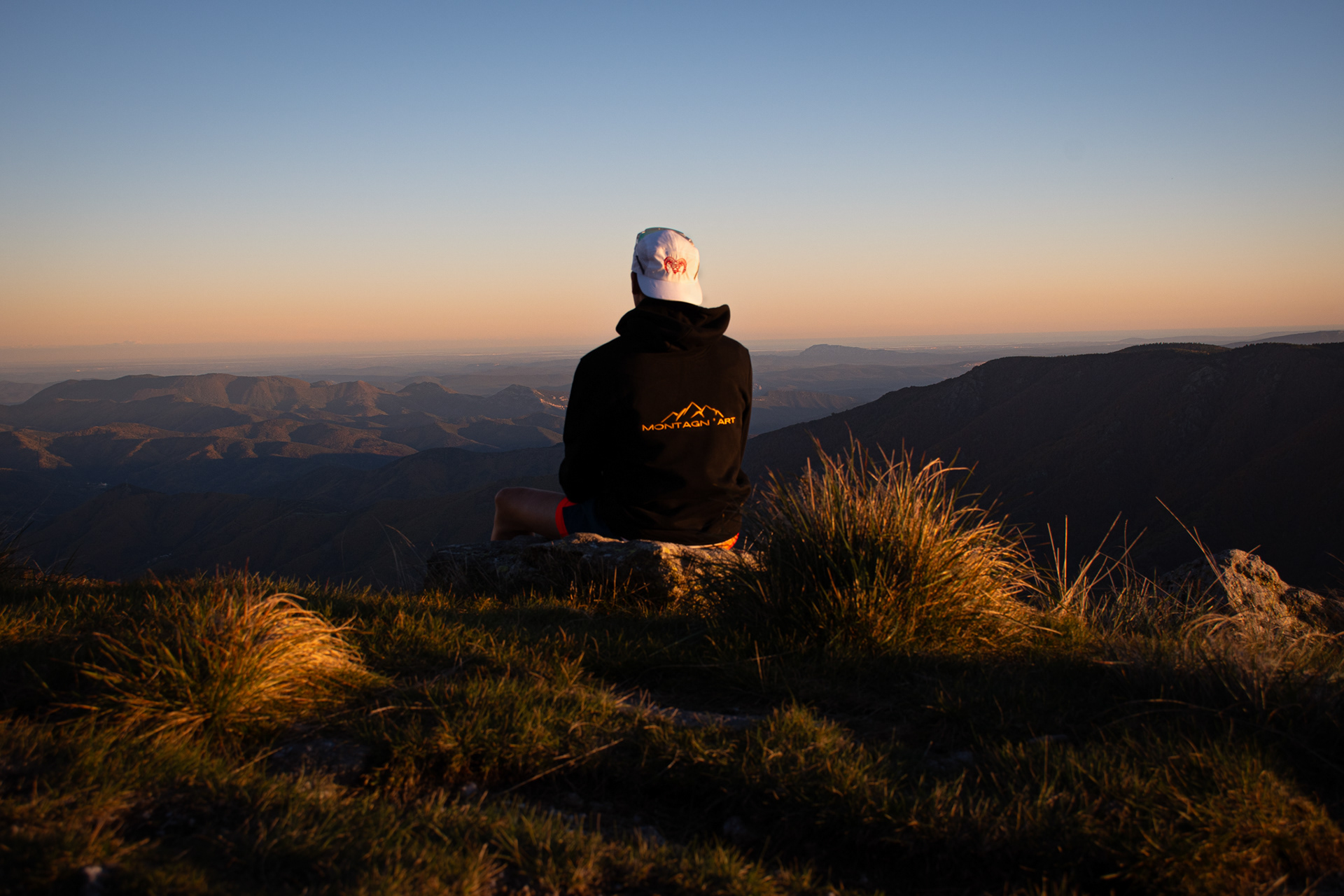 Séance Muflon au sommet, silhouette assise face au coucher de soleil, sweat Muflon by Montagn'Art
