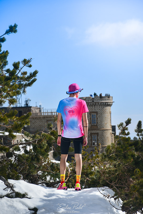 Séance Muflon en t-shirt dégradé rose et bleu, tour en pierre en arrière-plan, neige au sol