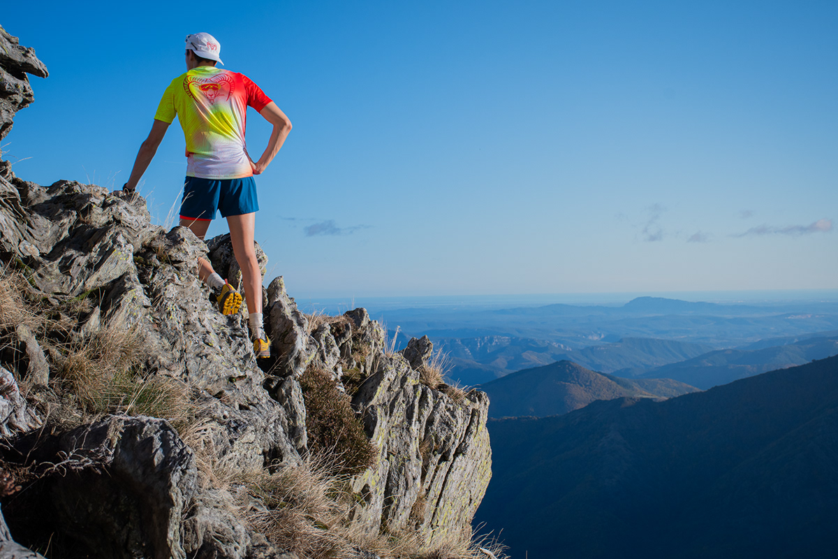 Coureur en t-shirt Muflon dégradé jaune et rouge sur une arête rocheuse