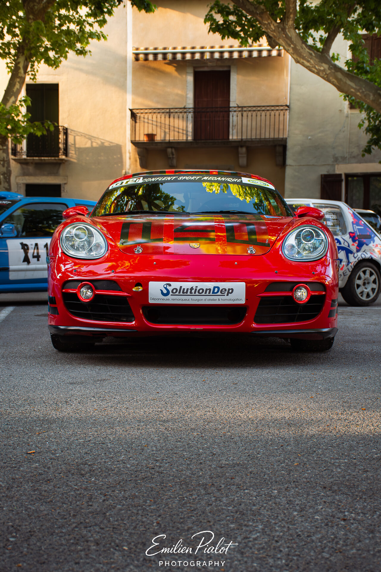 Porsche Cayman rouge vue de face devant une façade du village
